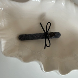 Detail of grey fabric hair clip with a small black bow and metallic logo on shell plate