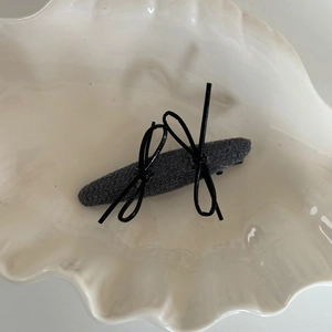 Minimalist dark grey fabric hair clip with black bows on a white ceramic shell tray