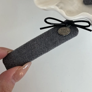 Close-up of grey tweed hair clip with black leather bow and silver metal logo plate