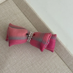 Detailed view of pink plaid bow hair clip with decorative pearls on beige fabric tray
