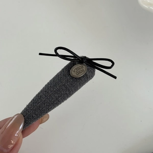 Elegant grey fabric hair clip with a black bow and vintage metal tag in a hand-held view