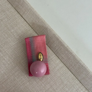 Close-up of pink plaid ribbon with a pearlescent bead and vintage 'love' metal charm
