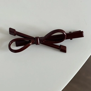Detailansicht einer kleinen weinroten Schleifen-Haarklammer mit glänzendem Finish und Metallclip