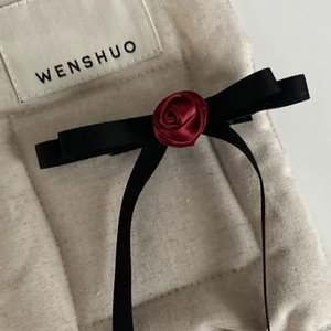 Detailed close-up of a black satin bow hair clip with a red fabric rose on linen fabric