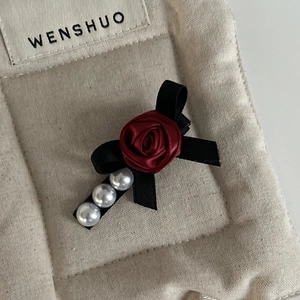 Close-up of elegant red satin rose hair clip with black bow and white pearls