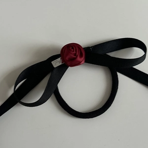 Detail of a black ribbon bow hair tie with red rose and a small silver metal tag