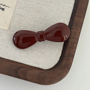Mini glossy red bow hair clip for side fringe on a wooden tray with canvas background