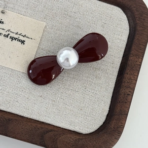Close-up of a mini red bow hair clip featuring a white pearl on a rustic wooden tray