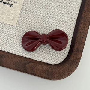 Close-up of a glossy deep red bow hair clip on a minimalist linen and wood background