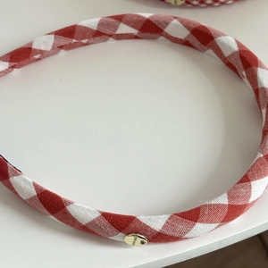 Close-up of red gingham headband featuring a round golden handmade metal tag