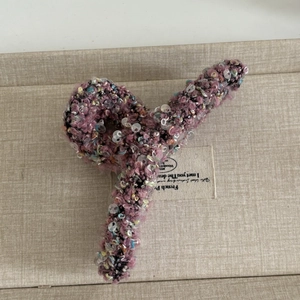 Détail d'une grande pince à cheveux en laine à paillettes roses et tissage texturé