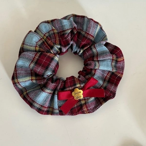 Détail du chouchou à carreaux rouge et bleu avec nœud en soie et plaque fleur dorée