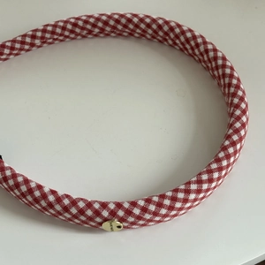 Detail of red and white gingham fabric headband with a gold handmade metal tag charm