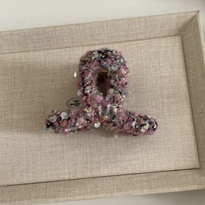 Détail macro de la grande pince à cheveux en tweed rose à paillettes sur fond texturé