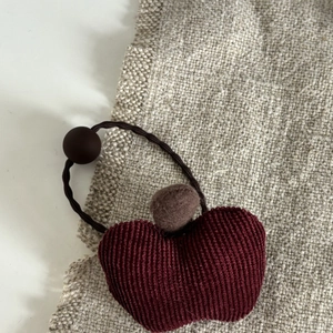Detail eines roten Cord-Apfel-Haargummis mit braunem Pompon und mattem Perlen-Accessoire
