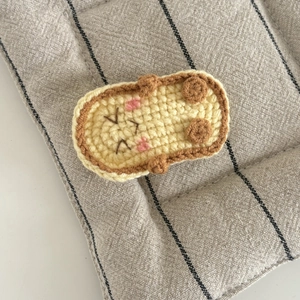 Nahaufnahme der handgestrickten Dackel-Haarspange in Creme mit braunen Kanten-Details