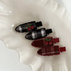 Détail de quatre barrettes à carreaux avec breloques cerise sur un plateau blanc