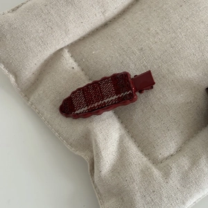 Détail d'une pince à cheveux vintage à carreaux rouges sur un support en tissu beige