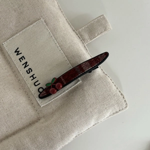 Détail de la pince à cheveux à carreaux rouges et noirs avec décor cerise 3D sur toile beige