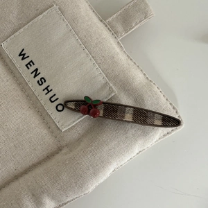 Détail d'une pince à cheveux à carreaux avec cerises 3D sur fond en toile beige
