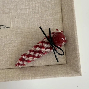 Close-up of red plaid tweed hair clip with pearl bead and black bow on beige texture
