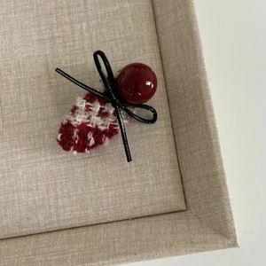 Detail of red and white tweed hair clip with a vintage dark red bead and black leather bow
