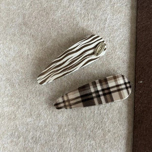Detailed view of two leopard and plaid hair clips featuring a gold-toned metal logo accent
