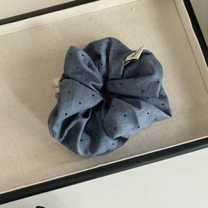 Close-up of blue polka dot fabric scrunchie with a white woven label in a grey tray