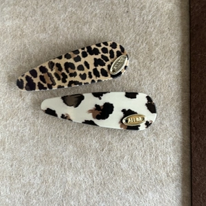 Set of two leopard and cow print acrylic hair clips with a gold brand tag on beige fabric
