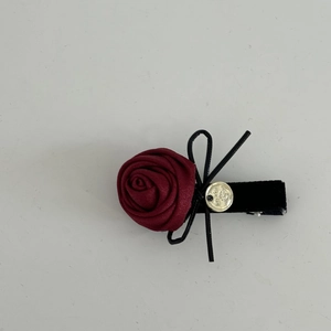 Détail d'une pince à cheveux rose rouge en soie avec nœud noir et emblème doré