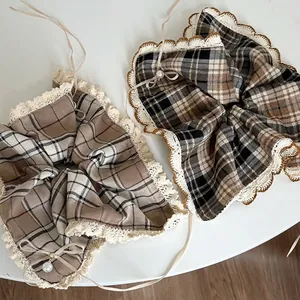 Brown plaid scrunchies with white lace trim, ribbon bows and pearls on a white surface