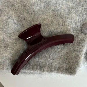 Glossy burgundy acetate hair claw clip for women on a soft grey textured fabric background