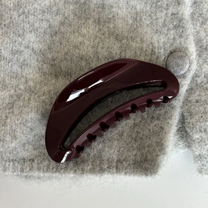 Macro detail of glossy dark red hair claw clip on soft grey knitted texture background