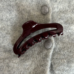 Close-up of a burgundy acetate hair claw clip on a grey knit sweater background