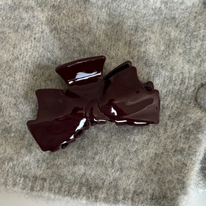 Close-up of a large burgundy acetate bow hair claw clip on a soft grey textured fabric