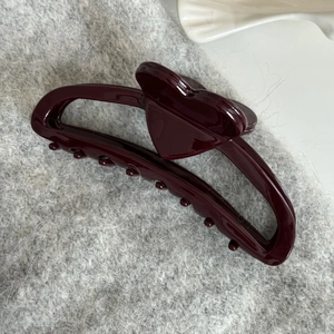 Close-up of a burgundy heart-shaped hair claw clip on soft grey knit fabric
