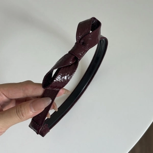 Detailed close-up of dark cherry red satin bow headband with glossy leather-like finish