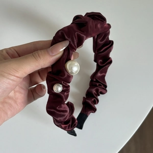 Close-up of cherry red pleated satin headband with elegant white pearl accents