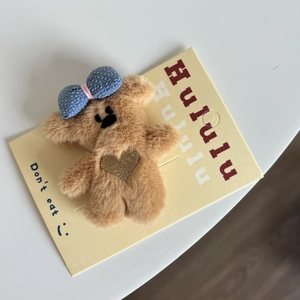Détail d'un accessoire ours en peluche marron avec nœud à carreaux bleu et broderie