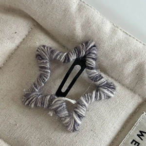 Détail macro d'une pince à cheveux étoile en laine mélangée gris-blanc sur tissu beige