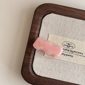 Close-up of pink wavy acetate hair clip on linen texture for Korean sweet style detail