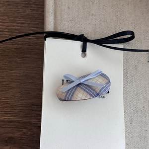Close-up of a blue plaid oval hair clip with a ribbon bow on a white display card