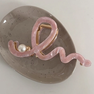 Detail of pink wavy acetate claw clip with pearl accent on a decorative ceramic tray