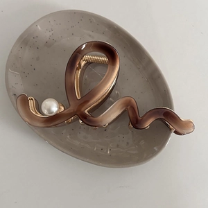 Brown wavy acetate hair claw clip with pearl detail on a ceramic tray display