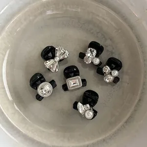 Détail de six mini pinces à cheveux noires avec strass et perles sur assiette céramique