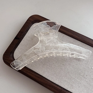 Close-up detail of a transparent hair claw clip with delicate white lace floral patterns