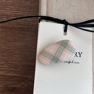 Detailed close-up of a pink and green plaid fabric oval hair clip on a wooden desk