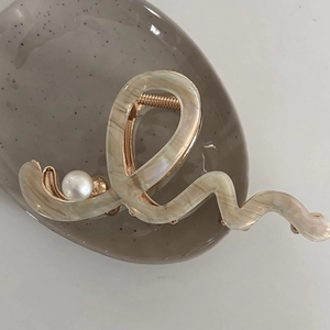 Detail of a wavy cream acetate hair claw clip with a white pearl and gold metal spring
