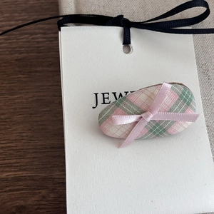 Close-up of pink ribbon bow on green checkered plaid hair clip on white card
