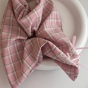 Close-up of pink plaid fabric accessory with floral lace edges and silky satin bows